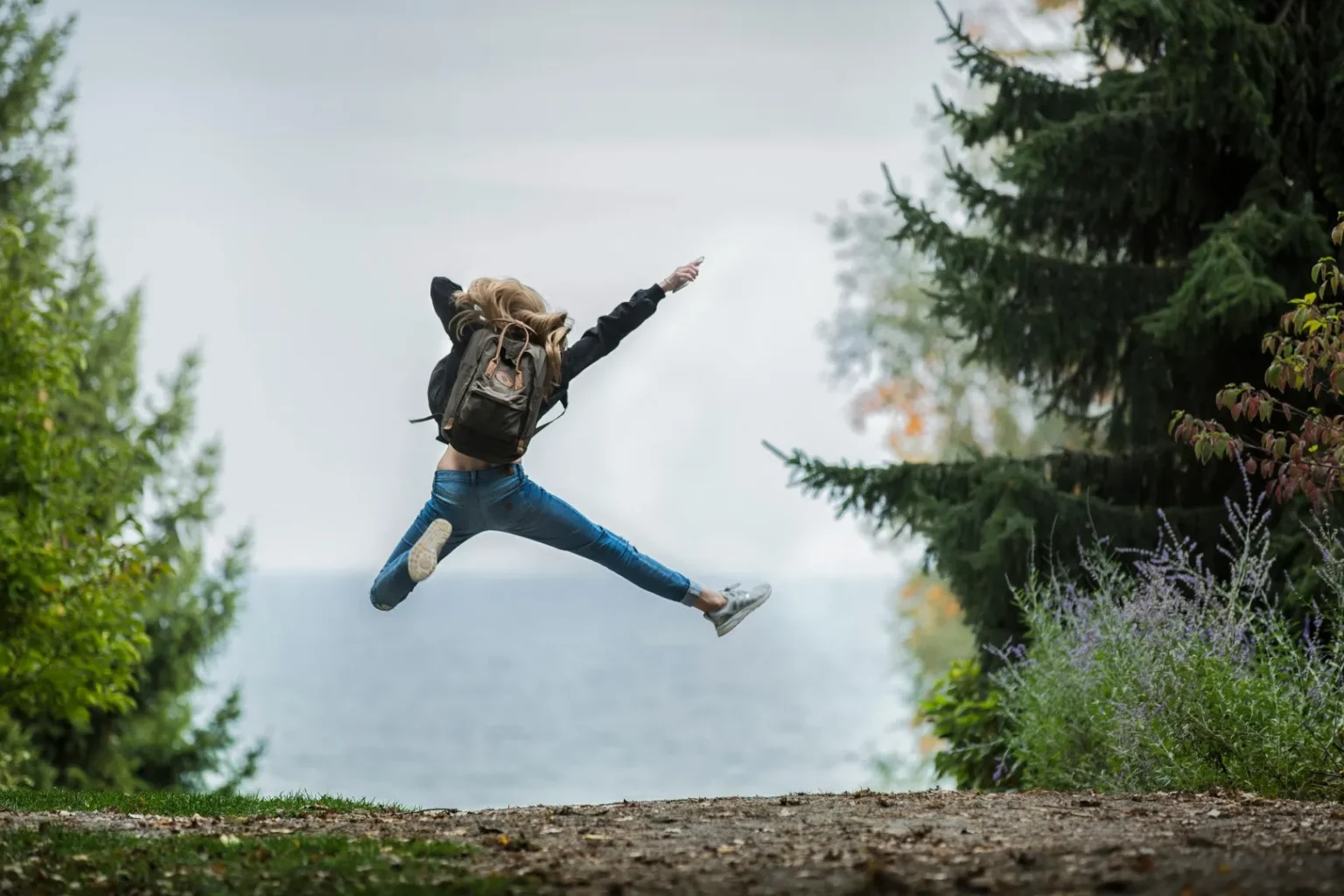 edukacja outdoorowa: uczeń z plecakiem skacze z radości na leśnej drodze