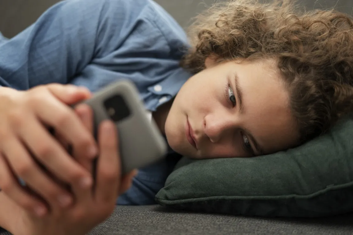 kobieta przegląda telefon przed snem w łóżku: zły nawyk prowadzący do uzależnienia od smartfona