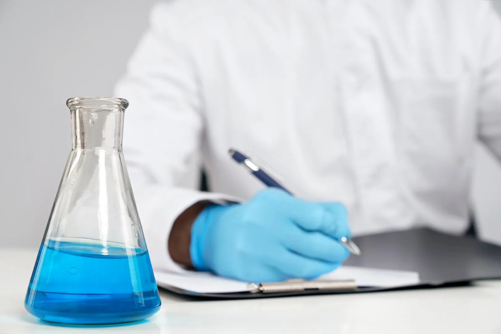 arkusze CKE z chemii rozszerzonej – osoba rozwiązuje zadania maturalne, w tle kolba chemiczna